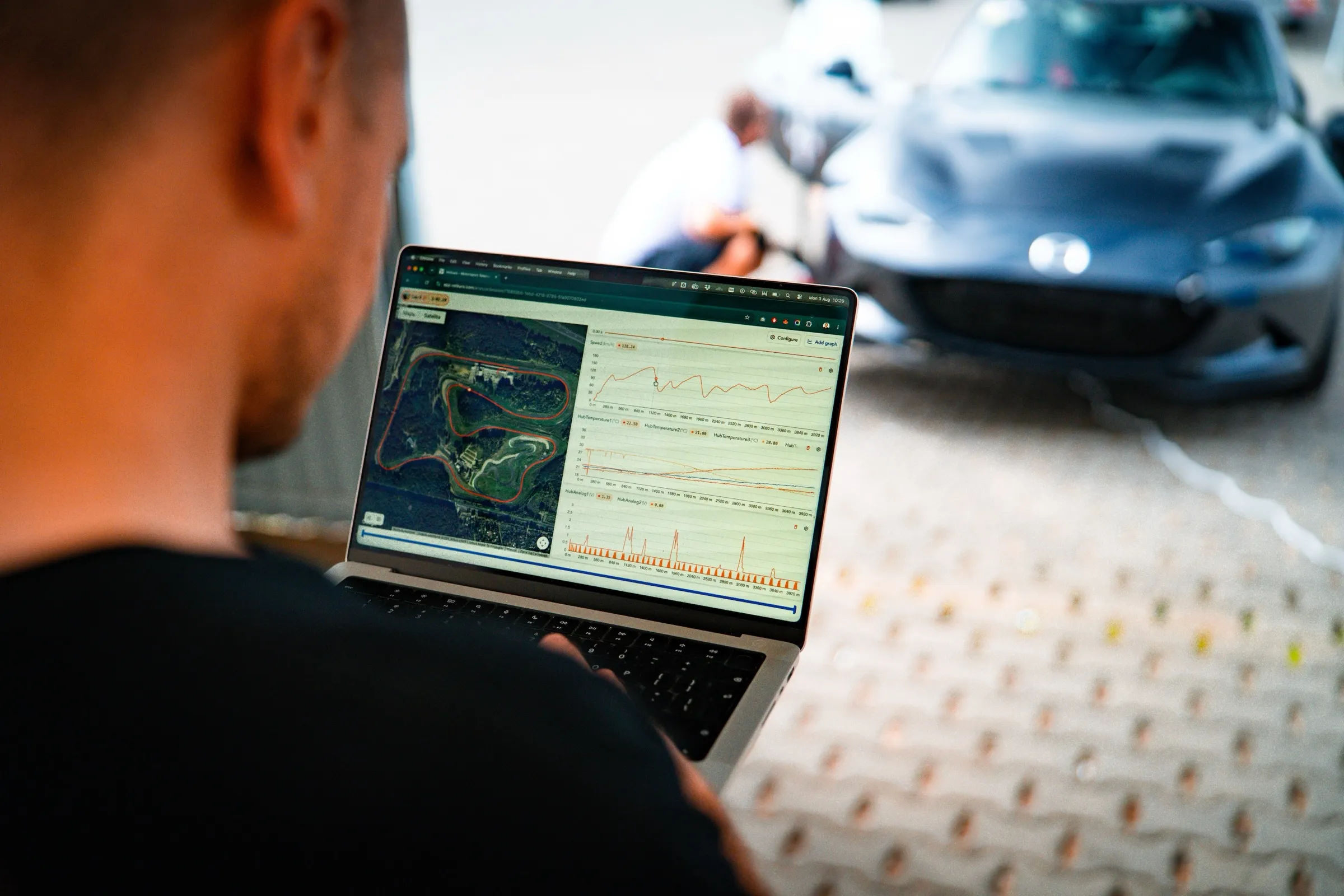 Kierowca przegląda w analizatorze Vetkuro mapę toru i wykresy z czujników, w tle Mazda MX-5 podczas dnia testowego